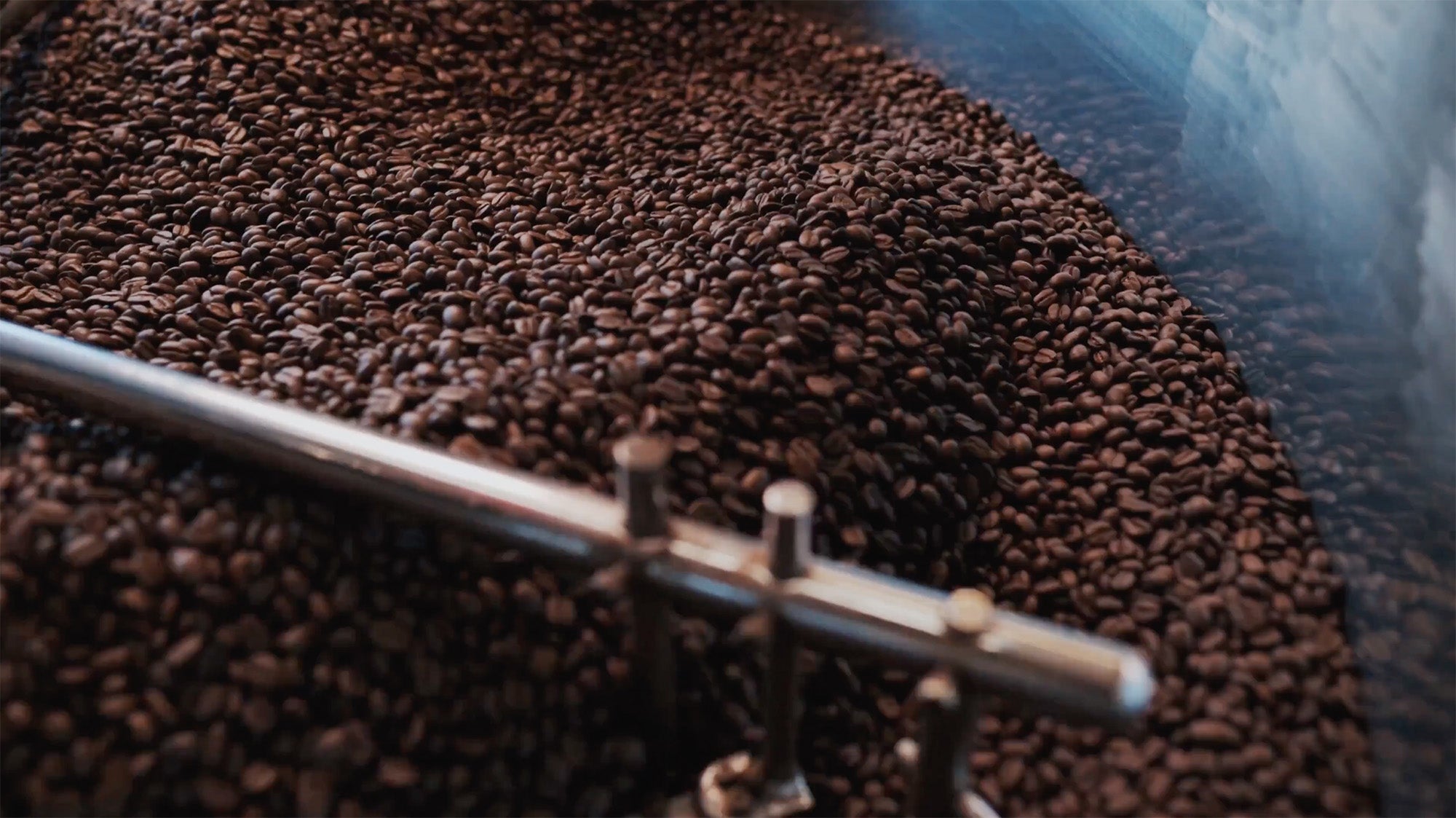 Load video: Close-up of coffee beans in an industrial rotating metal mixer