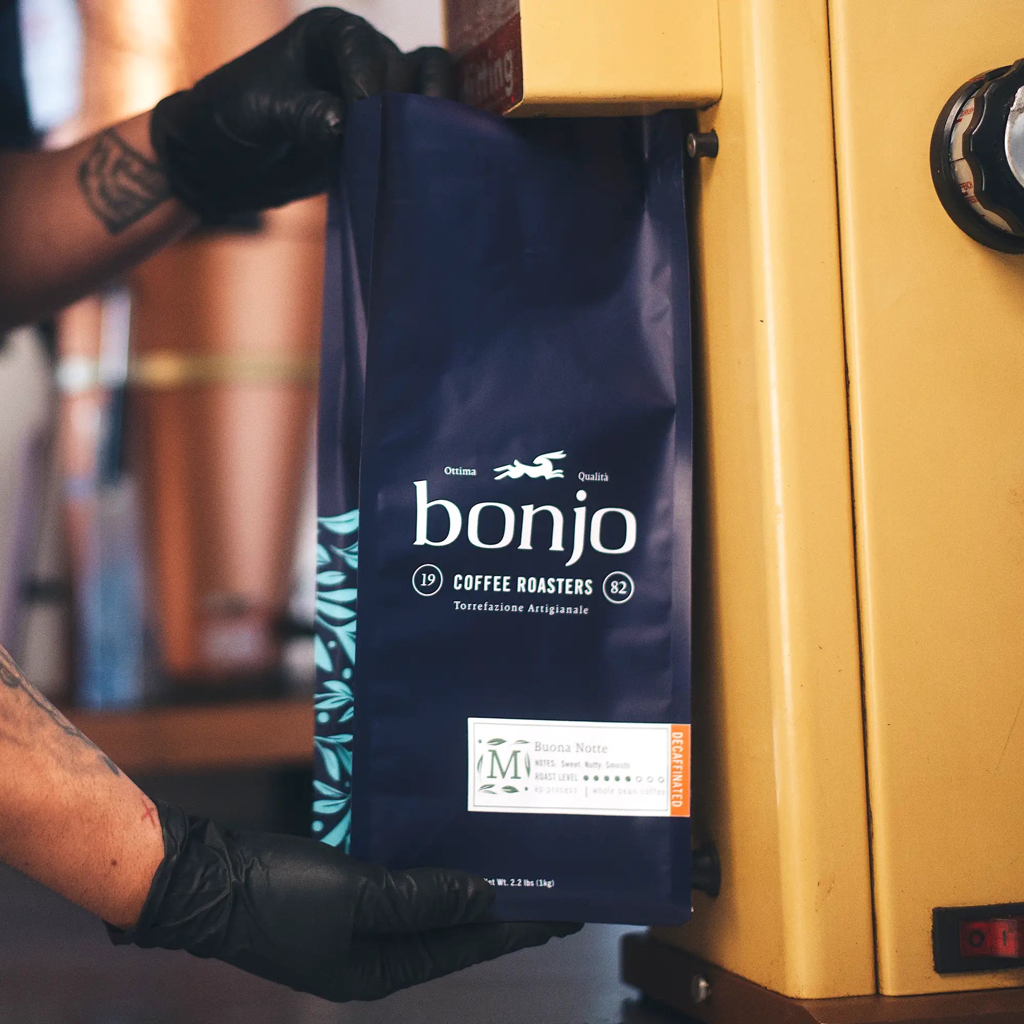 Person holding a blue bag of bonjo coffee roasters in front of a yellow machine.
