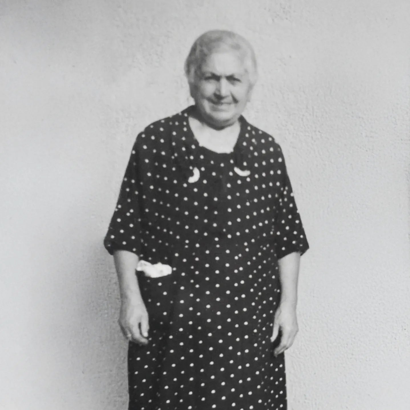 Black and white photo of an elderly woman wearing a polka dot dress against a plain background