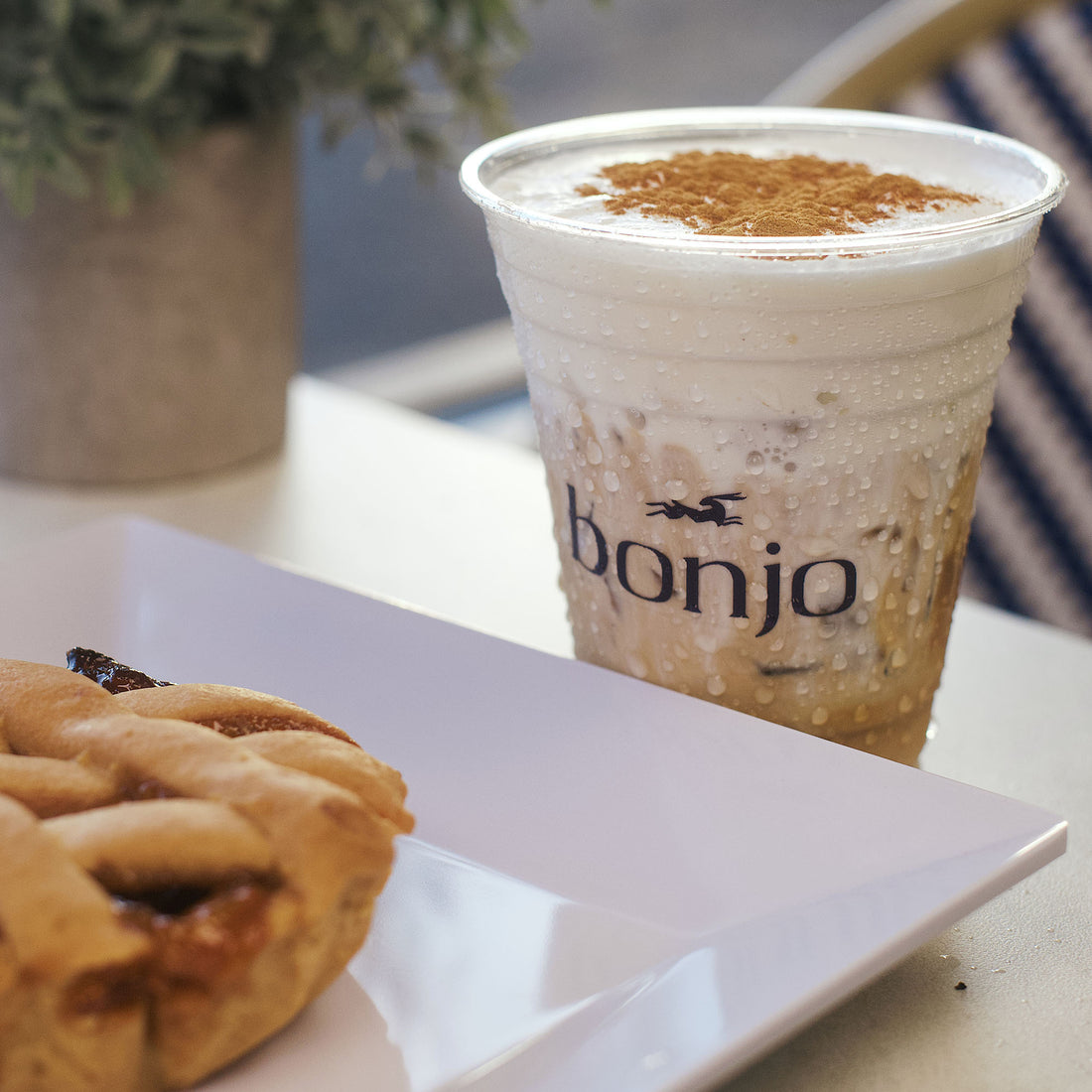 Cappuccino in a 'bonjo' cup with a pastry on a white plate.