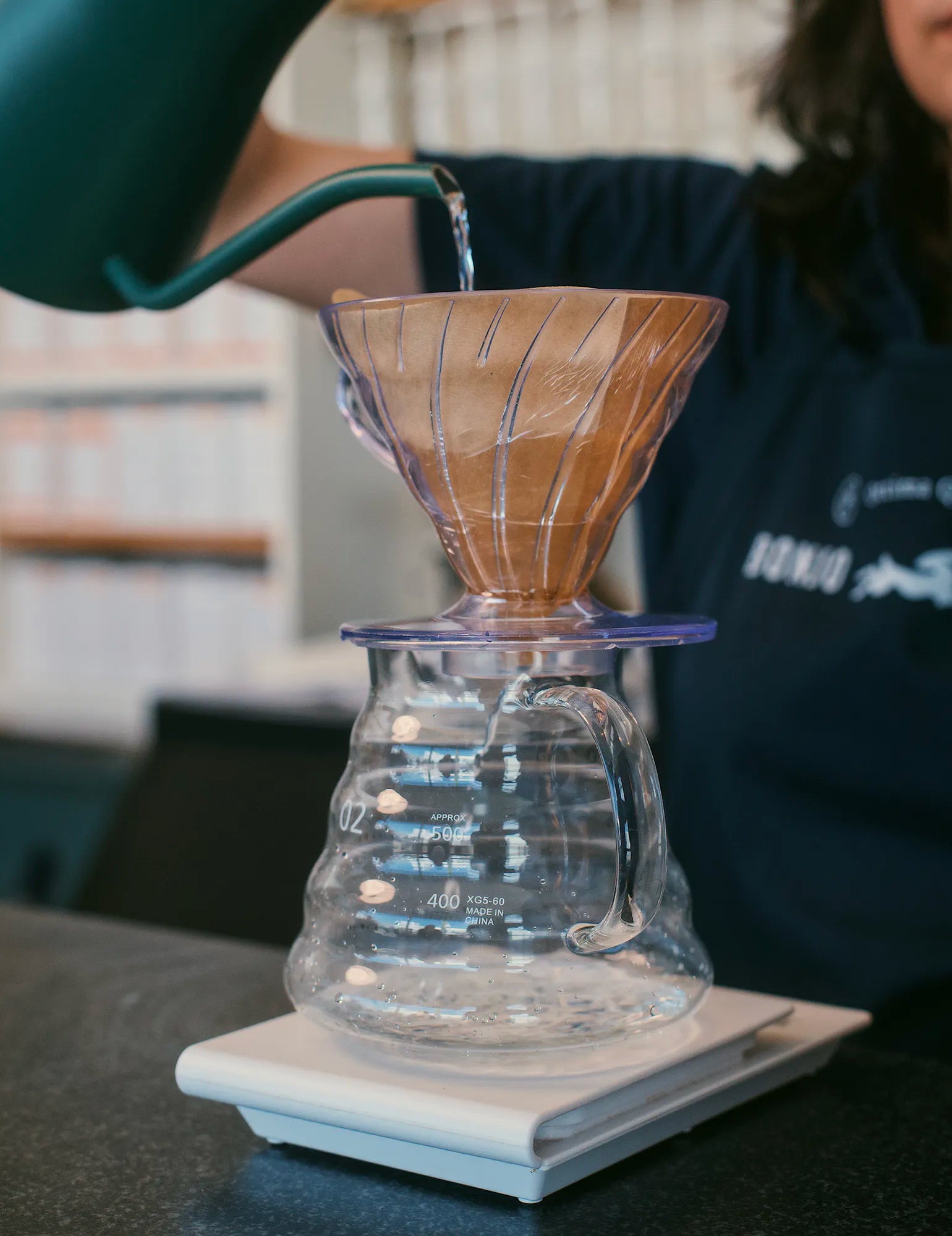 Person pouring water into a wooden coffee filter on a glass carafe.