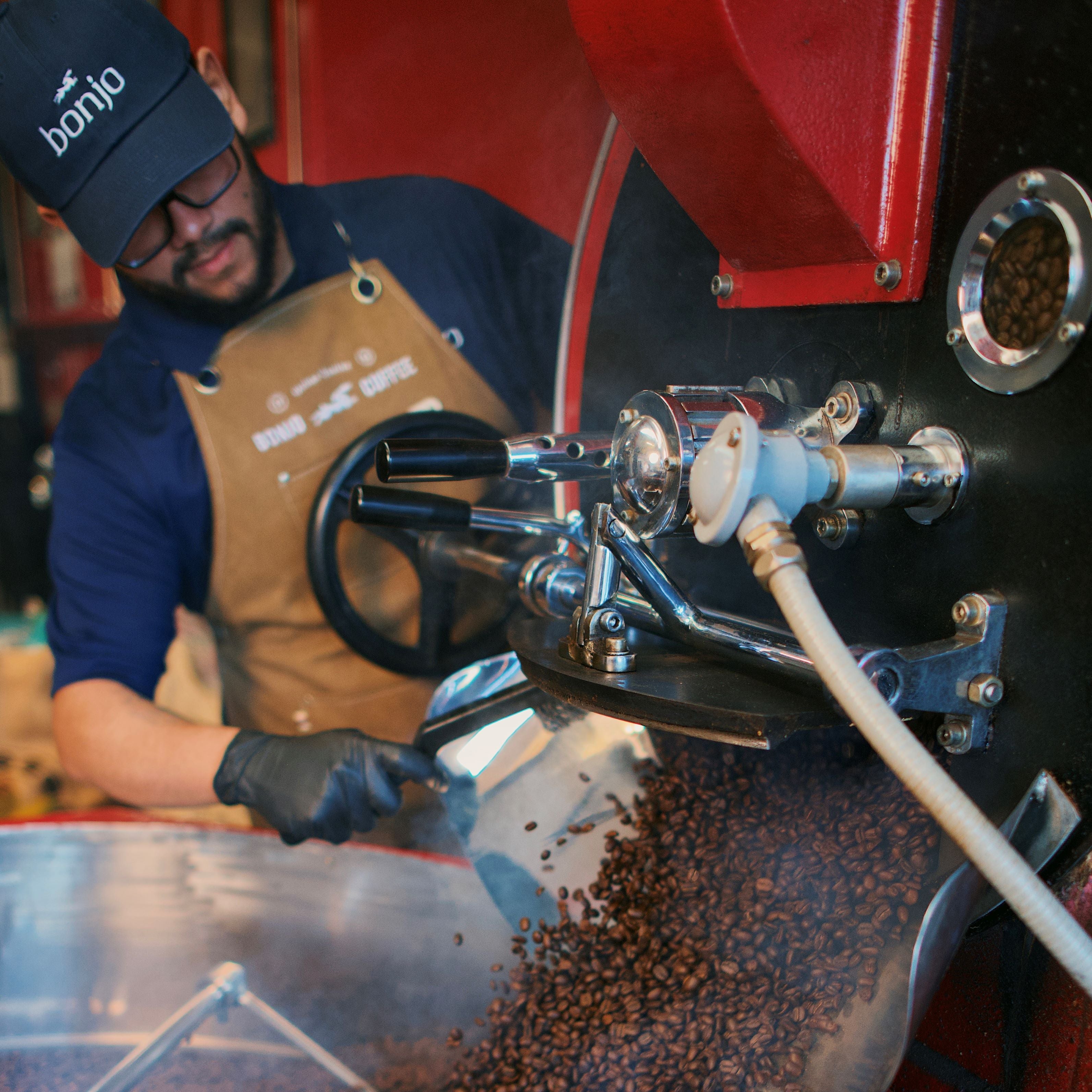Person operating a coffee roasting machine with coffee beans being processed.